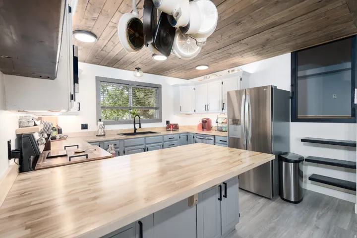 Kitchen featuring extensive wood-finish countertops, two-tone cabinetry with black hardware, stainless steel refrigerator, and wood plank ceiling