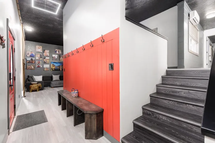 Entryway featuring light-toned wood-finish flooring, a vibrant red accent wall with integrated coat hooks, and a dark wood-finish staircase