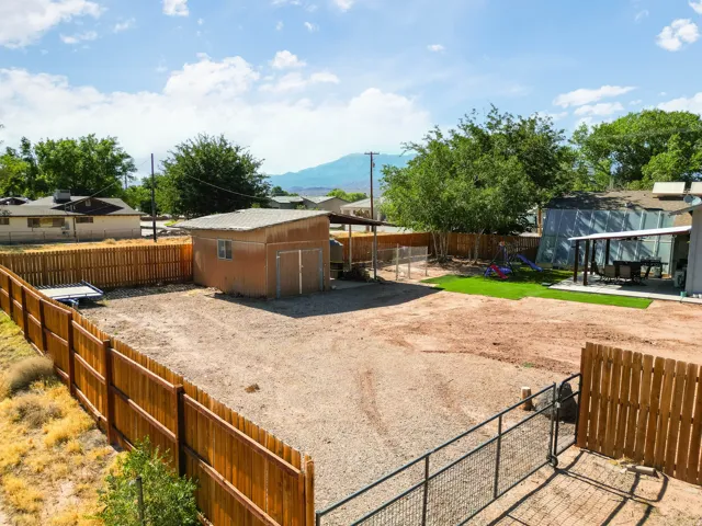 Expansive fenced backyard featuring a storage shed, gravel ground cover, and a dedicated artificial turf area with an attached patio cover