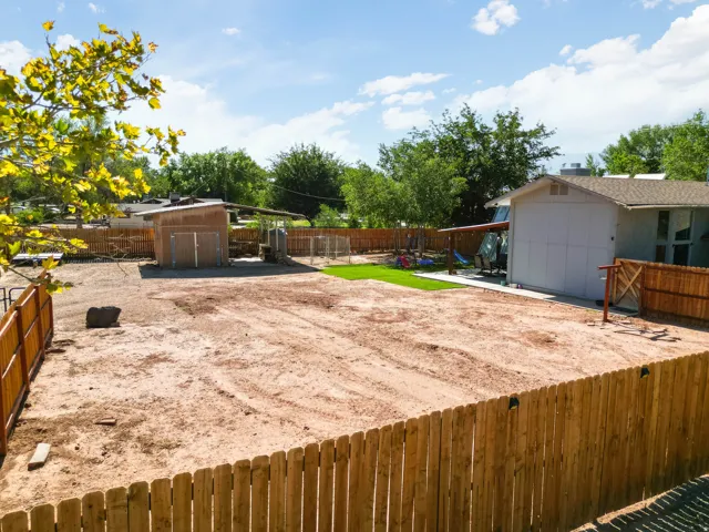 Expansive fenced backyard featuring a large cleared area, a separate storage shed, a covered patio, and a small artificial turf section