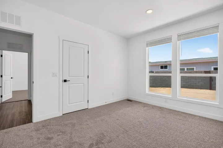 Light-filled room featuring neutral-toned carpet, recessed lighting, and a white interior door with matte black hardware