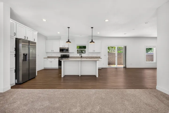 Open-concept kitchen featuring white cabinetry, stainless steel appliances, an island with seating, and wood-finish flooring