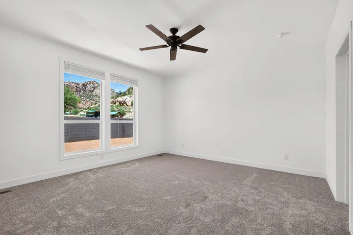 Spacious room featuring neutral carpeting, white walls, and a dark-toned ceiling fan