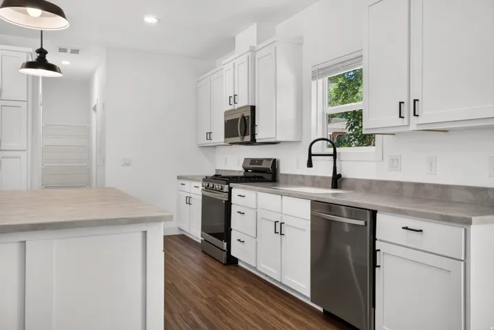 Bright kitchen featuring white shaker cabinetry, stainless steel appliances, dark wood-finish flooring, and light-toned countertops