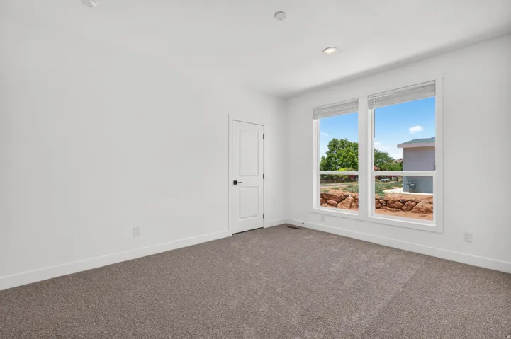 Carpeted room with white walls, two large windows, and a white two-panel door with black hardware