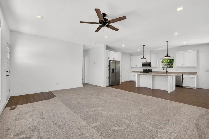 Open-concept living space featuring a contemporary kitchen with white cabinetry, stainless steel appliances, and a central island with pendant lighting
