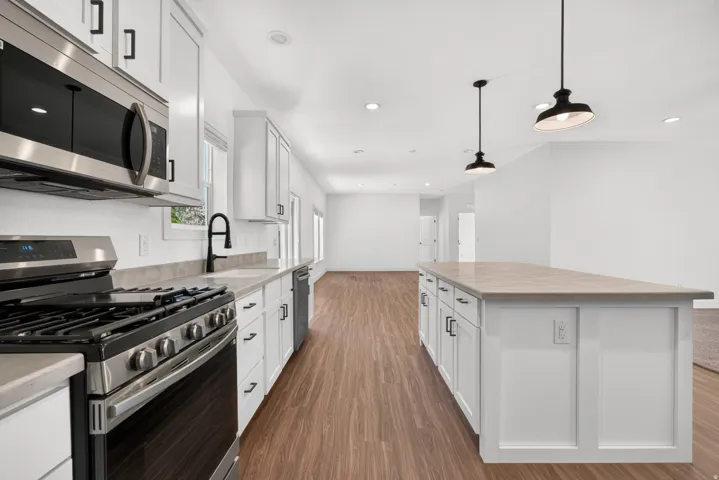 Kitchen featuring white cabinetry with dark hardware, stainless steel appliances, a gas range, and a kitchen island with pendant lighting