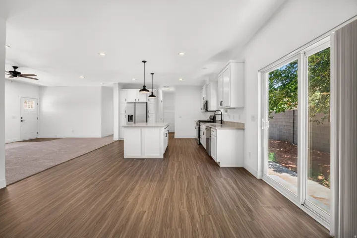 Modern kitchen featuring white cabinetry, a central island with pendant lighting, stainless steel appliances, and wood-finish flooring