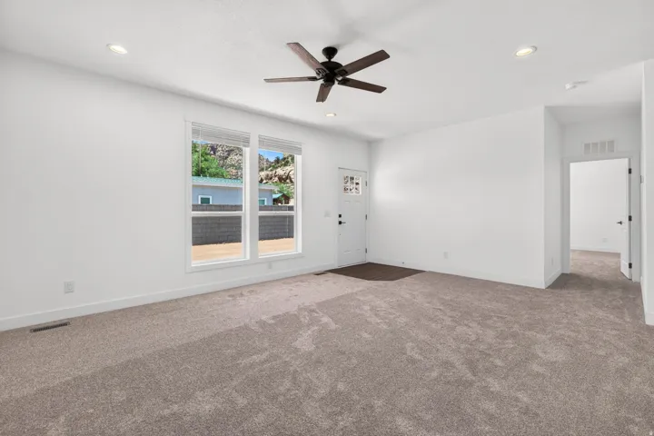 Spacious room featuring new carpet flooring, recessed lighting, and a dark-toned ceiling fan