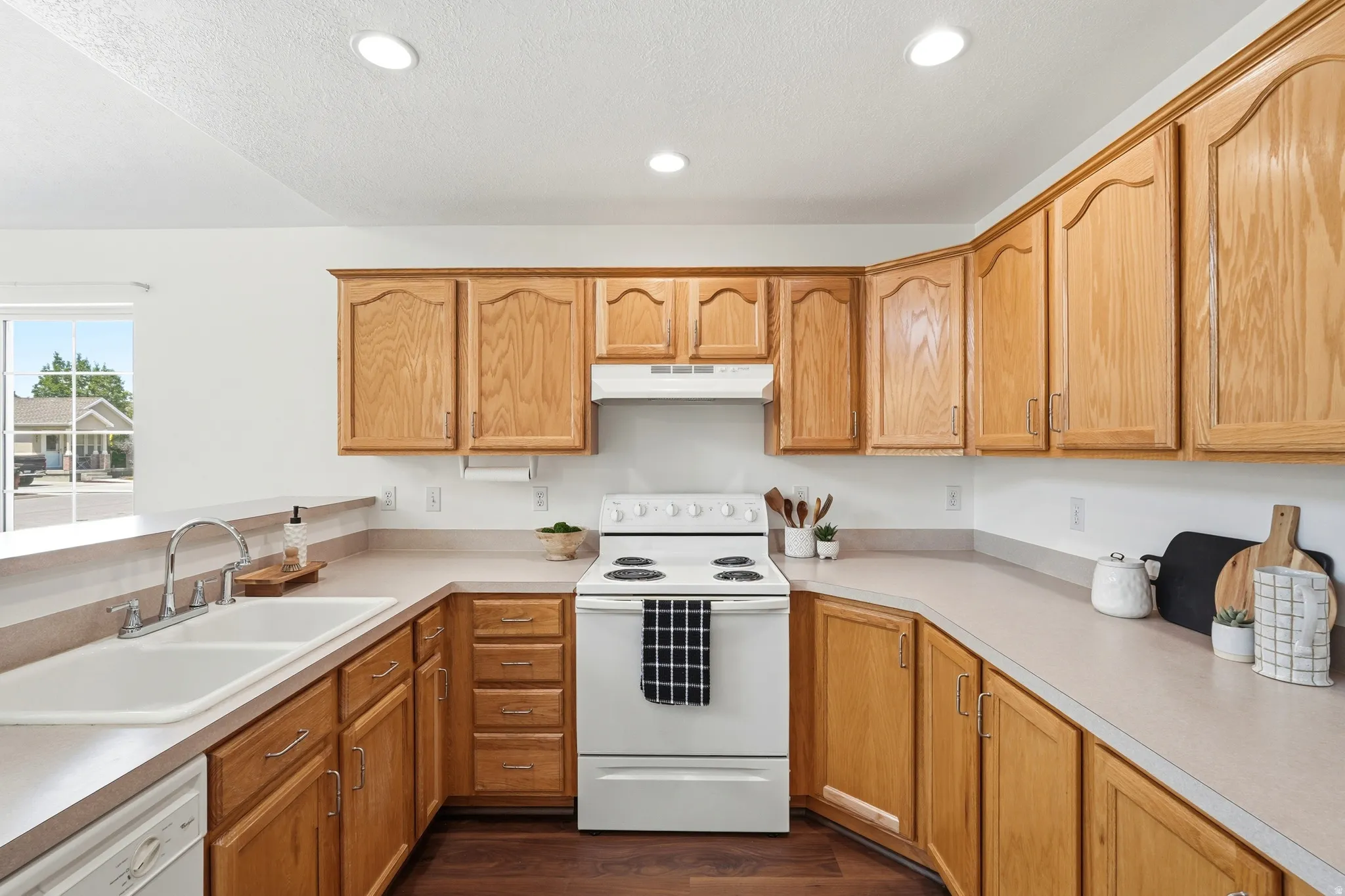 Kitchen featuring wood cabinetry, solid surface countertops, a double basin sink with chrome faucet, a white range, and recessed ceiling lighting