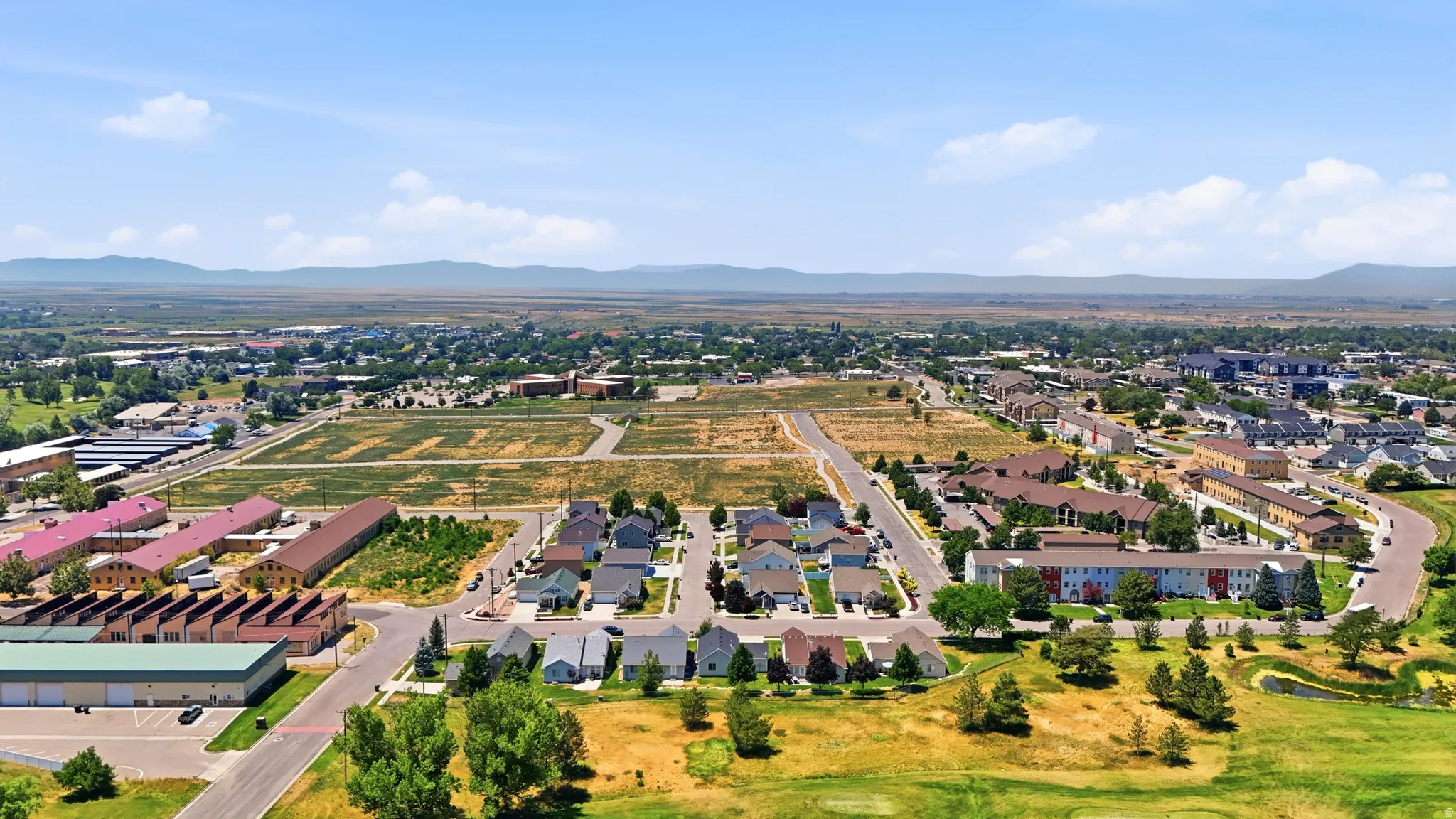 Expansive community showcasing residential developments, varied architectural styles, open land parcels, and distant mountain ranges under a clear sky