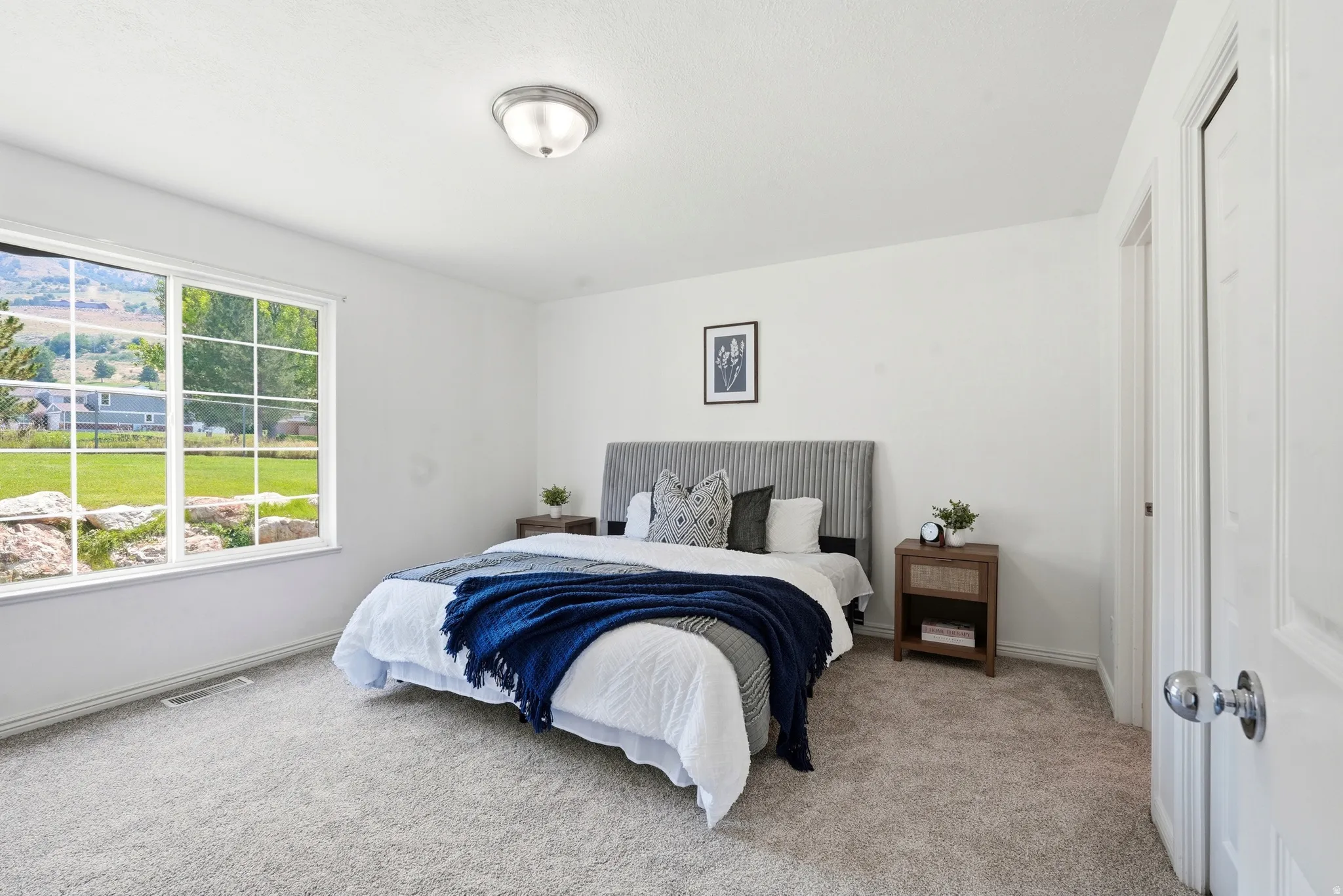 Bright bedroom featuring a large window, plush carpet flooring, white walls, and a ceiling-mounted light fixture