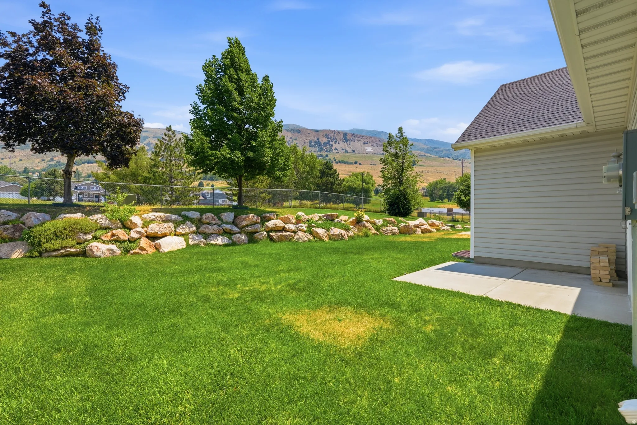 Expansive grassy yard featuring a stone retaining wall and mature trees