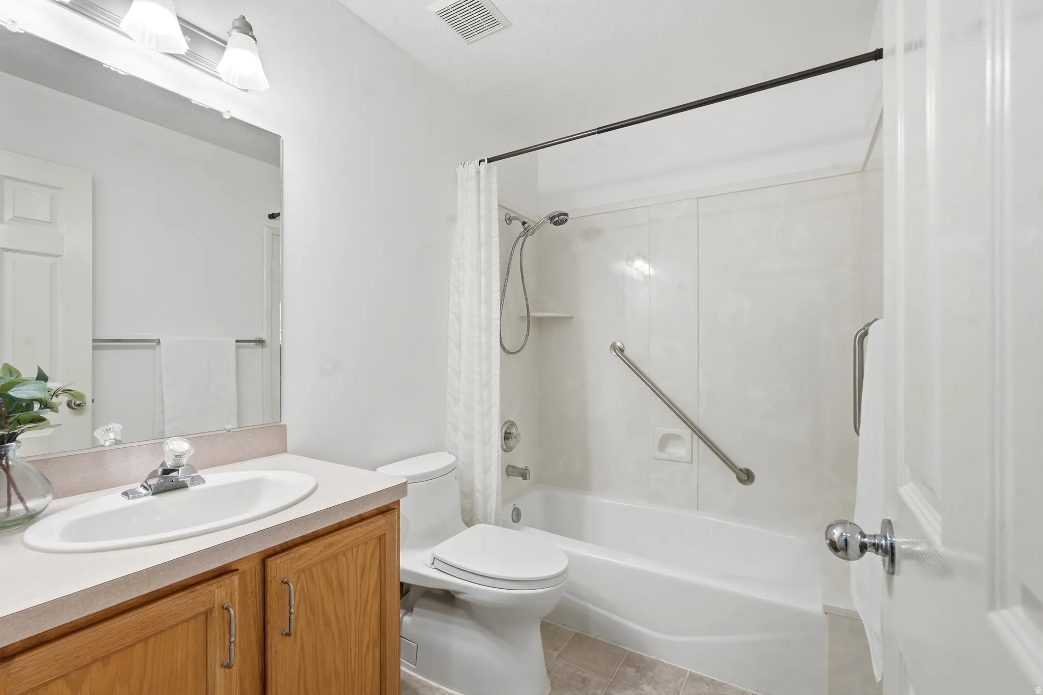 Full bathroom featuring a single vanity with wood-finish cabinetry, a toilet, and a combination tub and shower with grab bars