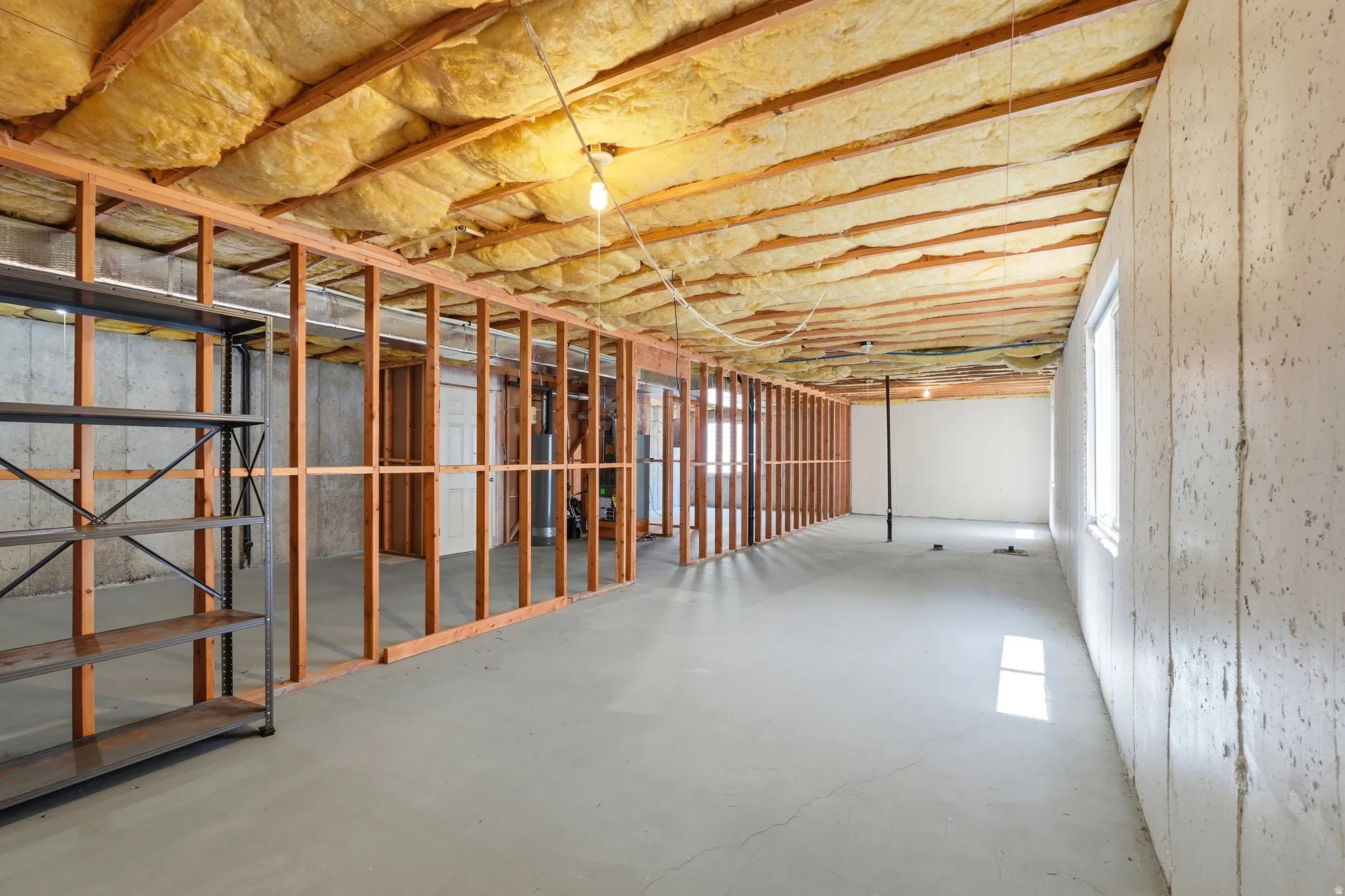Unfinished basement featuring wood framing, exposed insulation, a concrete floor, and multiple windows