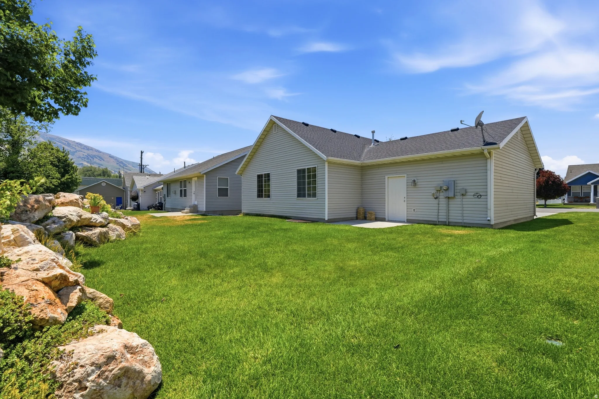 Expansive green lawn with a rock retaining wall and garden beds