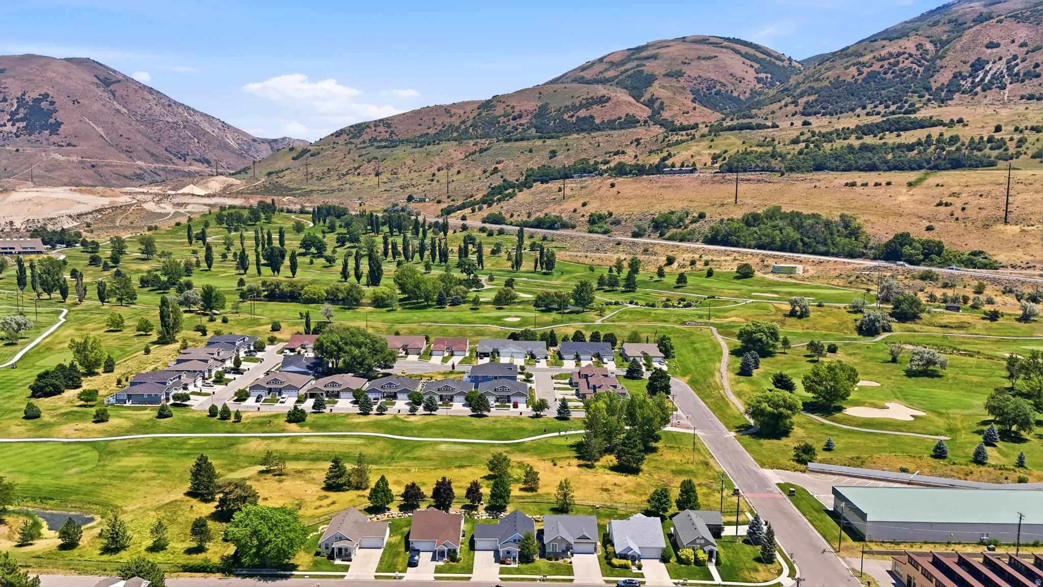 Residential community set against a mountainous backdrop, featuring a golf course, mature trees, and paved roadways