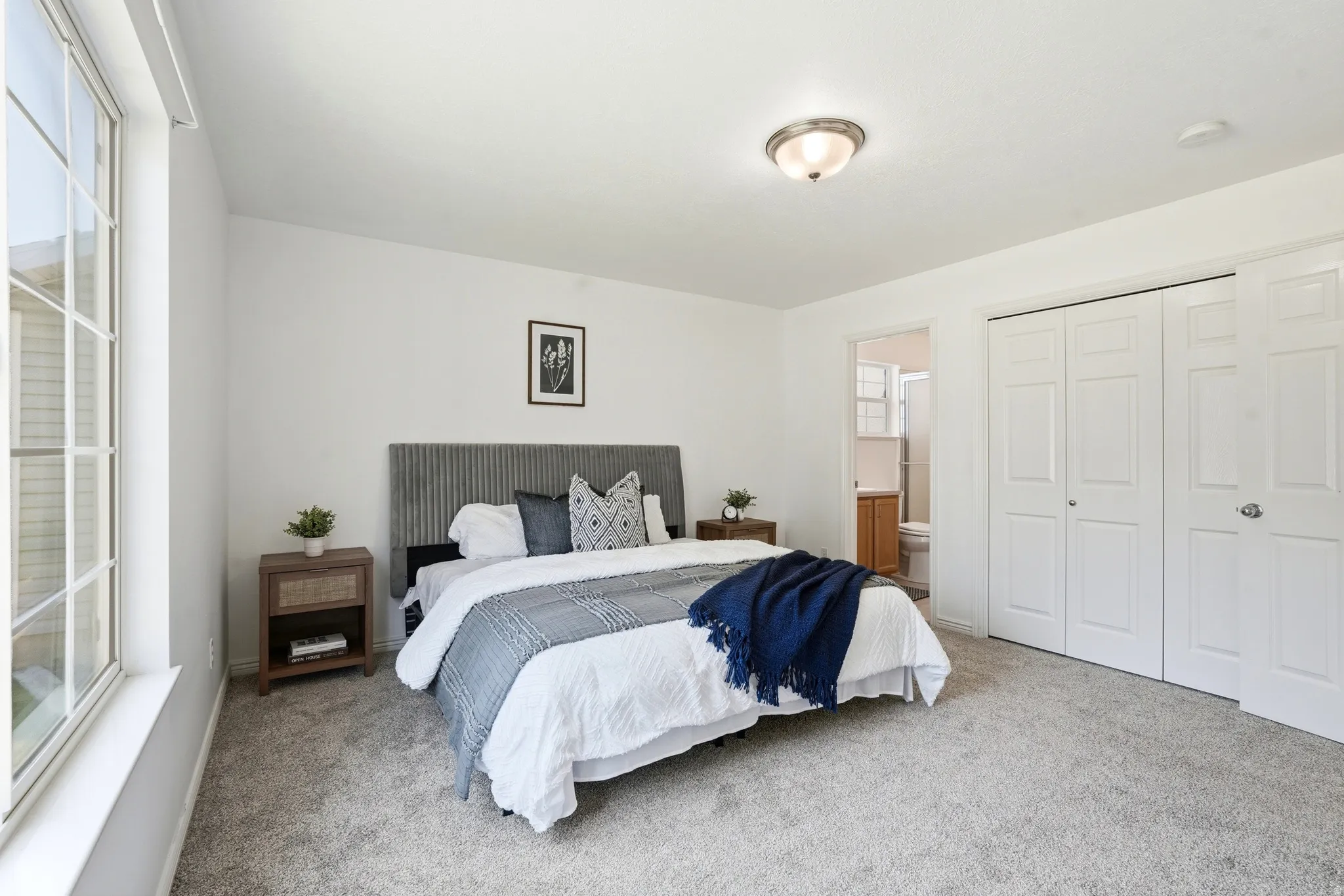 Spacious room featuring light gray carpeting, neutral wall paint, a large window, a ceiling-mounted light fixture, and closet with bifold doors
