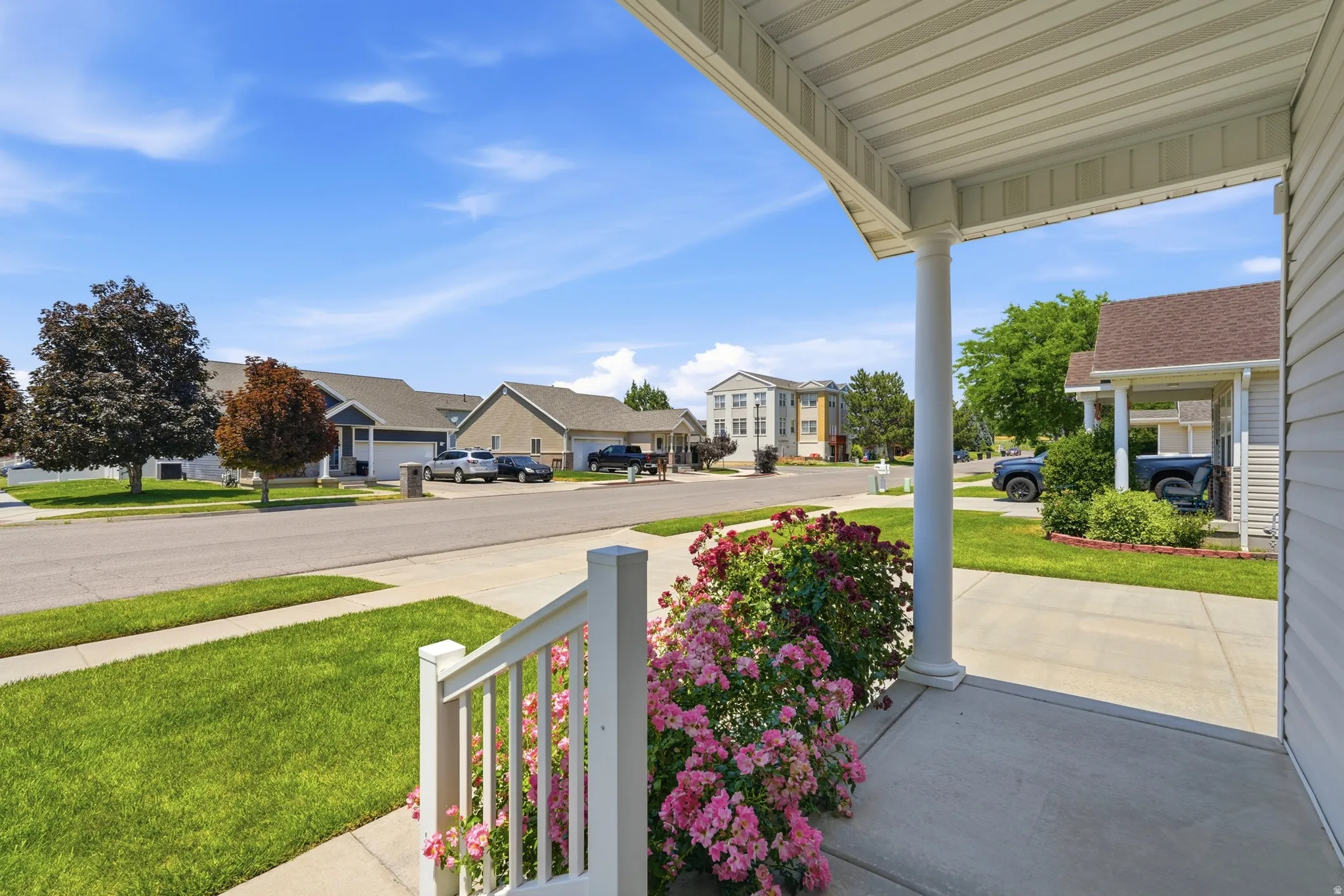 Inviting front porch with a white column and railing, bordered by a vibrant rose bush