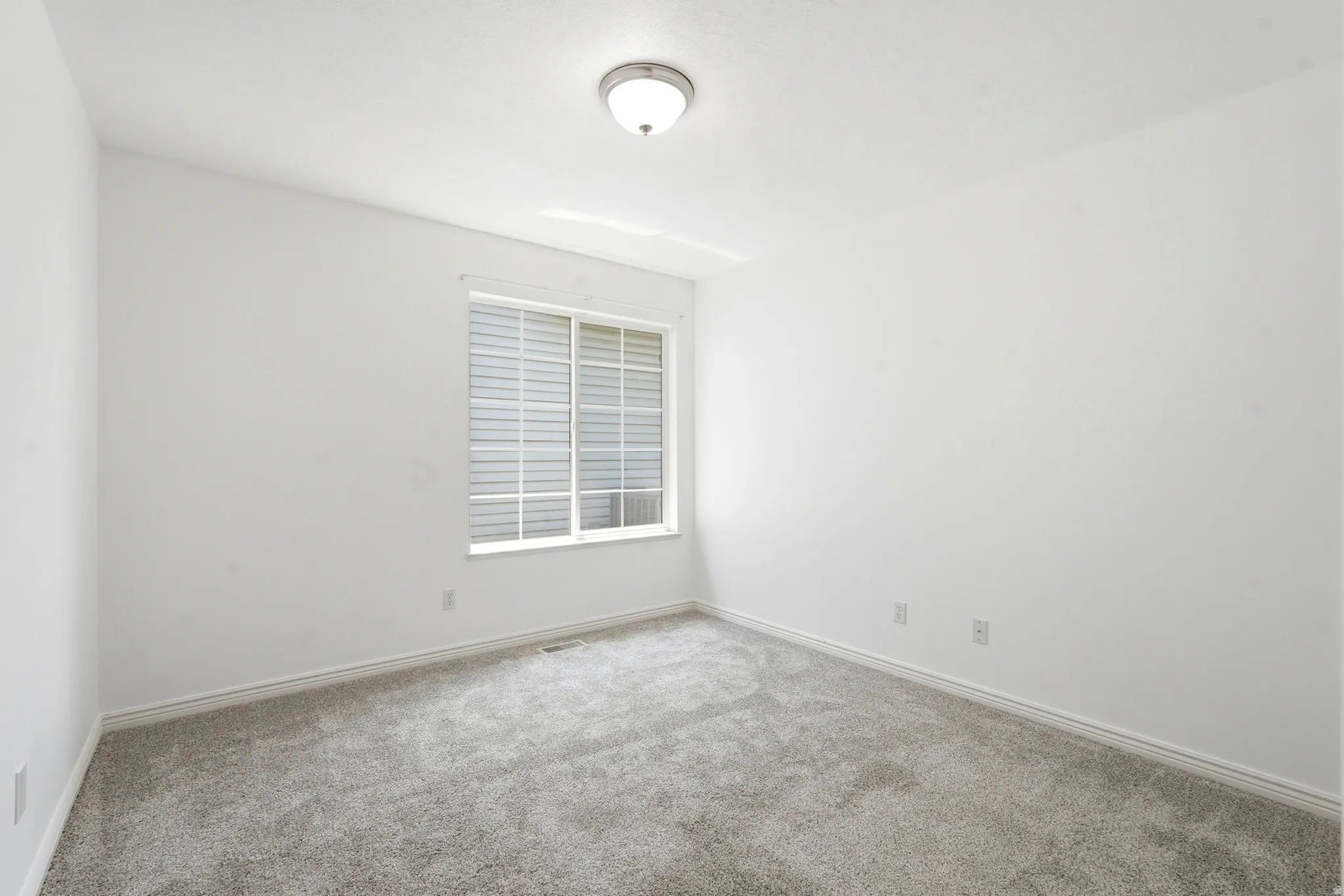 Carpeted room with white walls, a white-framed window with blinds, and a flush-mount ceiling light fixture