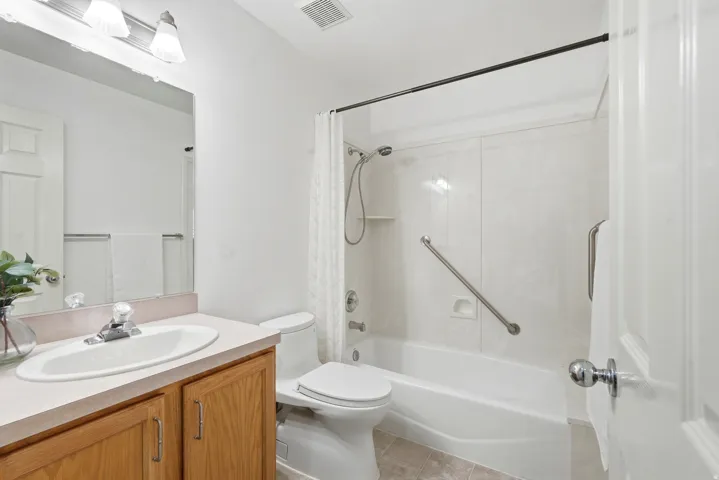 Full bathroom featuring a single vanity with wood-finish cabinetry, a toilet, and a combination tub and shower with grab bars