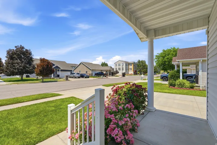 Inviting front porch with a white column and railing, bordered by a vibrant rose bush