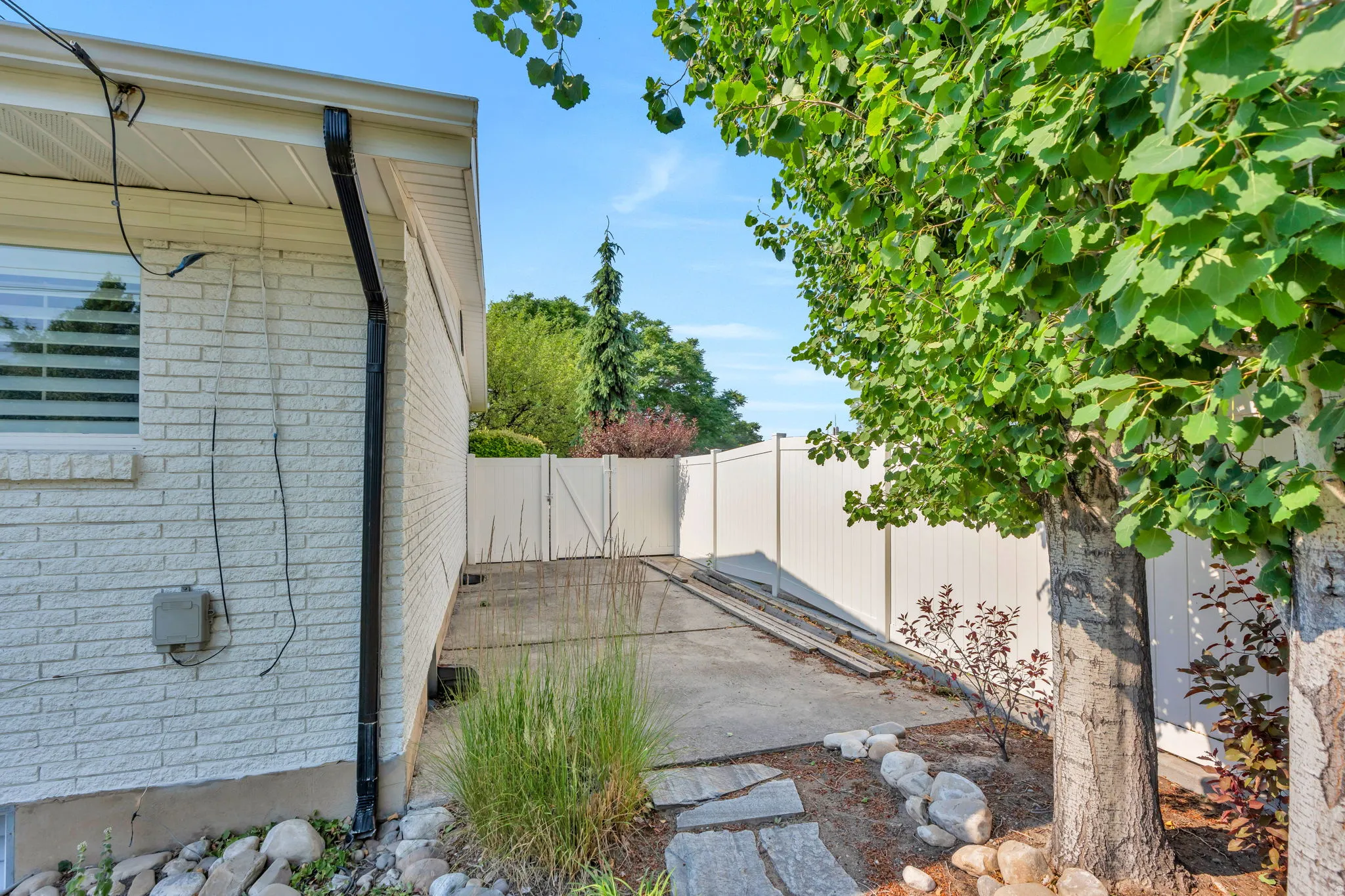Paved outdoor patio with a white privacy fence, mature trees, and a light brick exterior