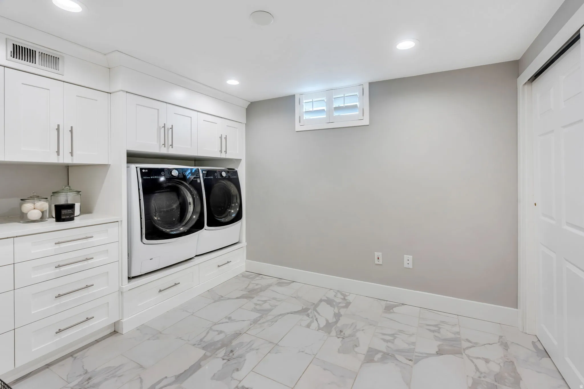 Large laundry area featuring extra deep white shaker cabinetry, quartzite countertops, and pedestal risers