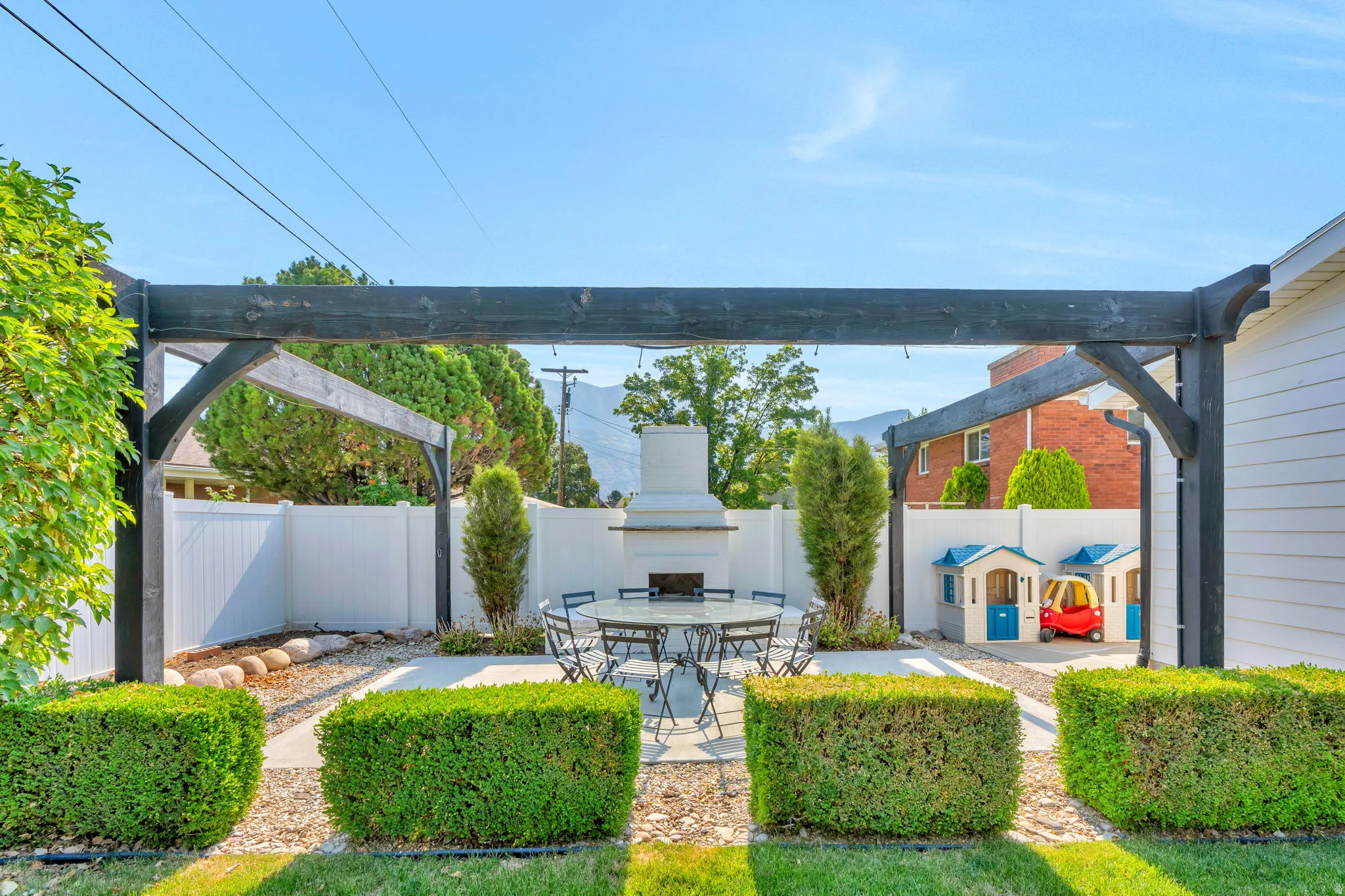 Outdoor living space featuring a dark-stained wood pergola over a concrete patio with stone fireplace.