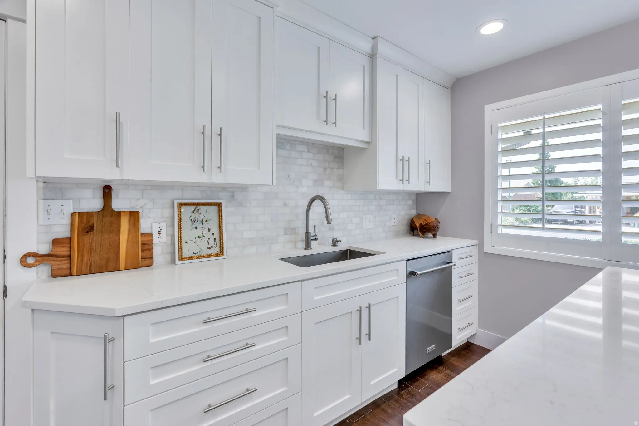 Modern kitchen featuring white shaker cabinetry with brushed nickel pulls, white quartzite countertops, and a marble backsplash