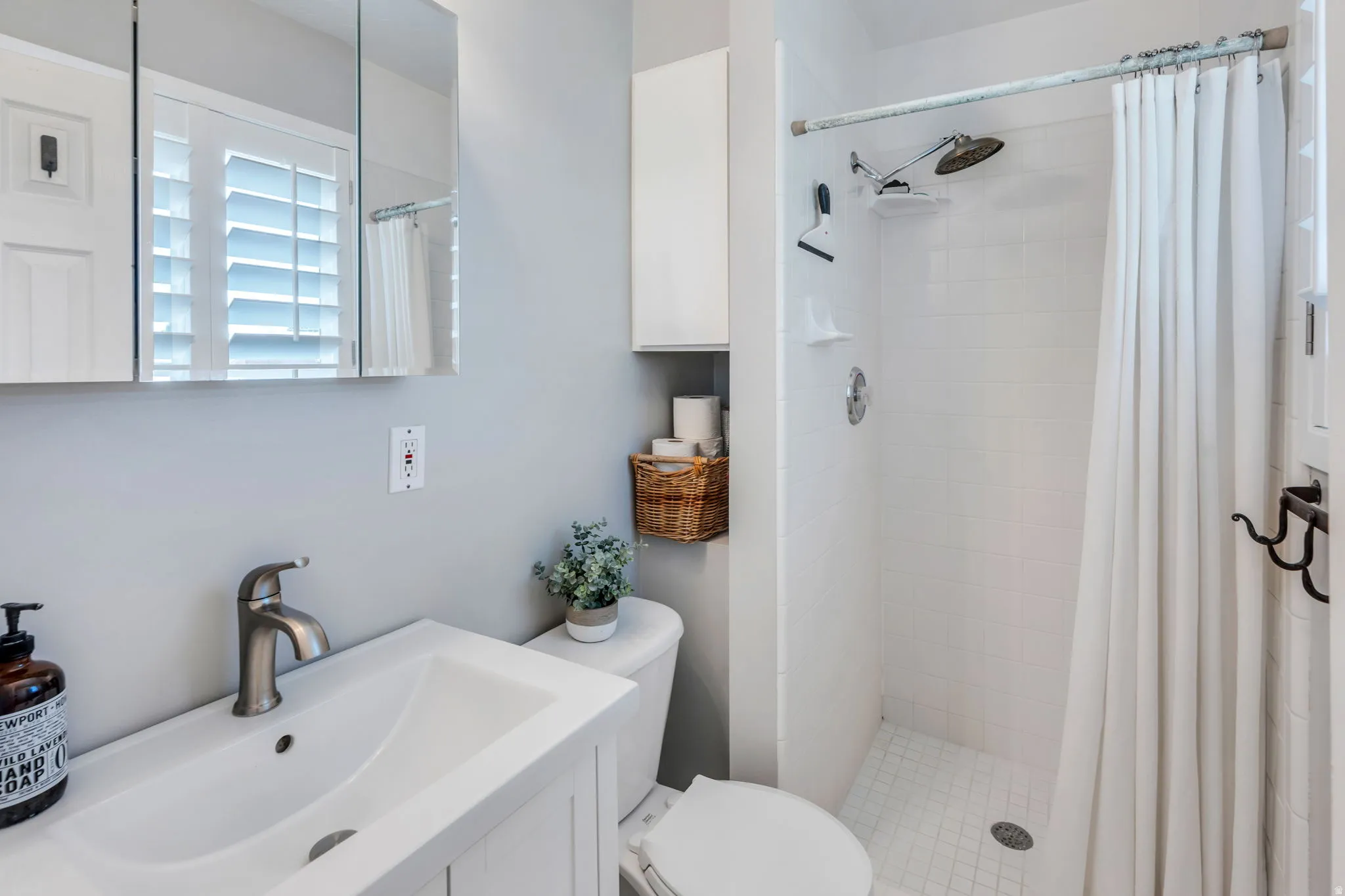 Primary Bathroom featuring a white vanity with integrated sink, brushed nickel faucet, and a tri-fold mirrored medicine cabinet