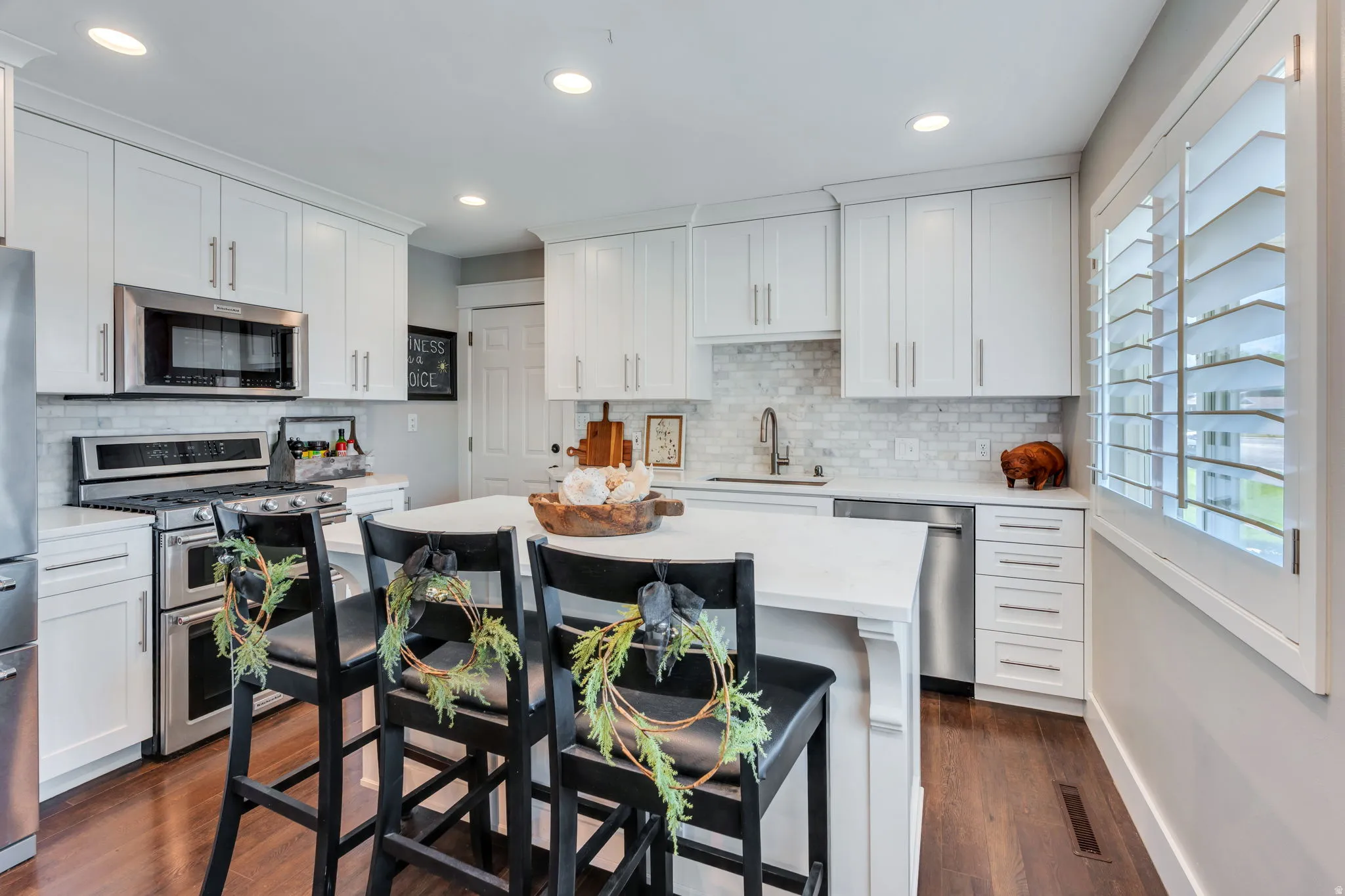 White kitchen featuring stainless steel appliances, a white tile backsplash, light countertops, and dark wood-finish flooring