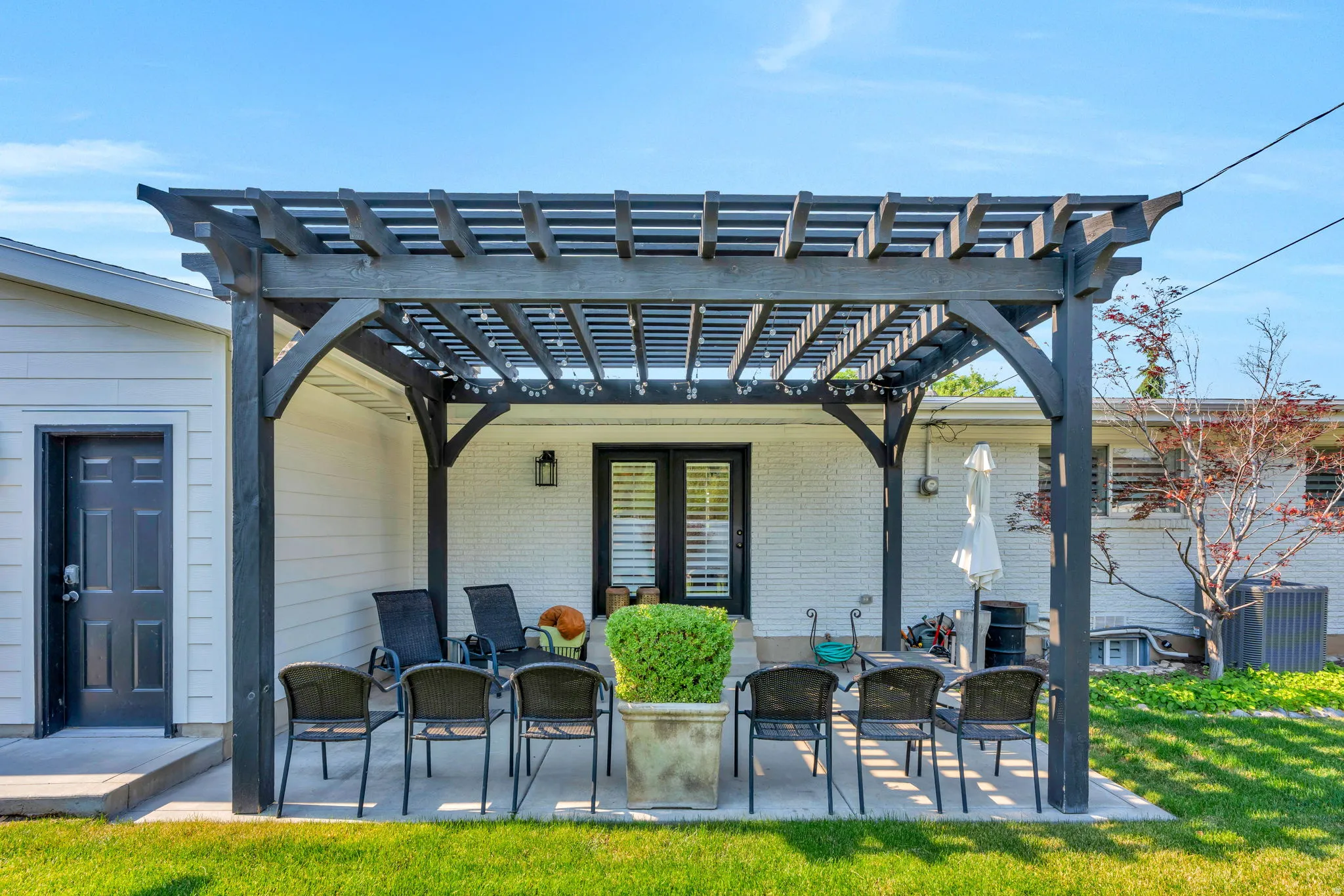 Expansive patio featuring a dark wood pergola, concrete slab, and manicured lawn