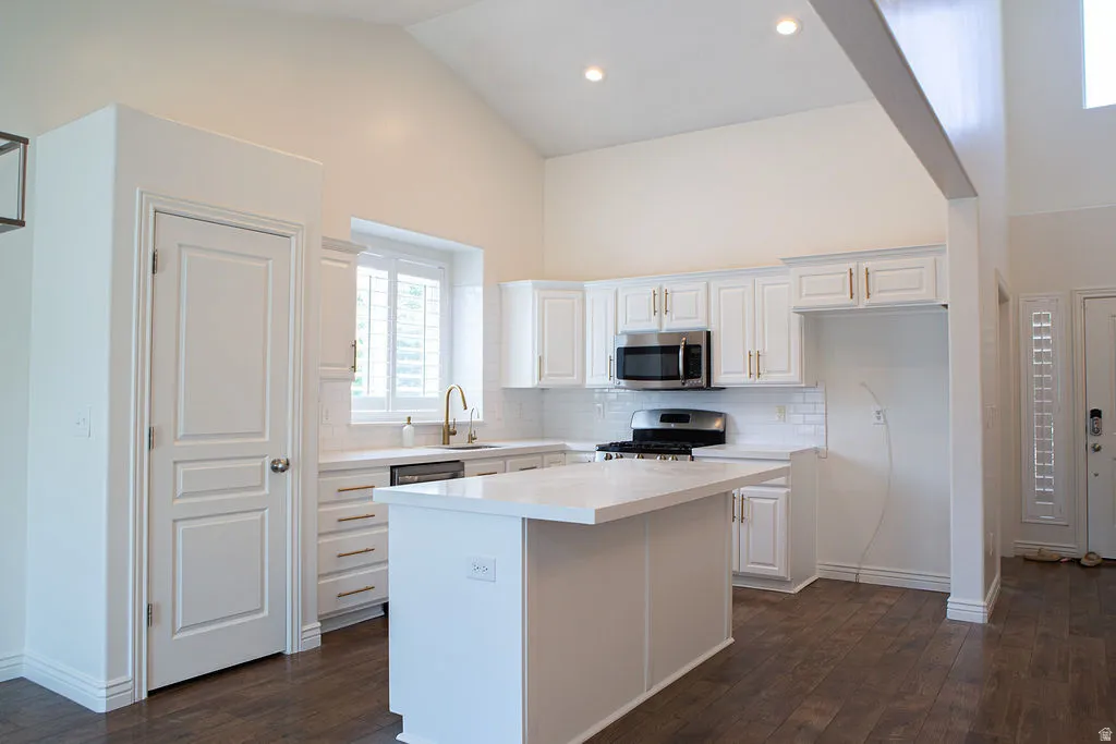 Vaulted kitchen ceiling with recessed lighting, featuring a central island, white cabinetry, integrated microwave, and a gas range