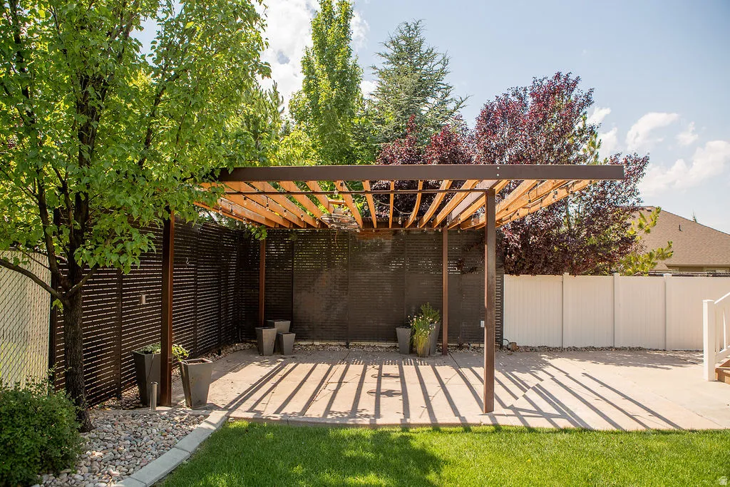 Outdoor entertaining area featuring a contemporary pergola with slat roof, privacy fencing, and a concrete paver patio