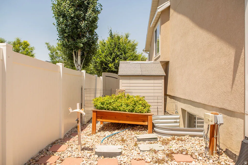 Enclosed patio area featuring a light-toned privacy fence, a wooden planter box with greenery, and a storage shed
