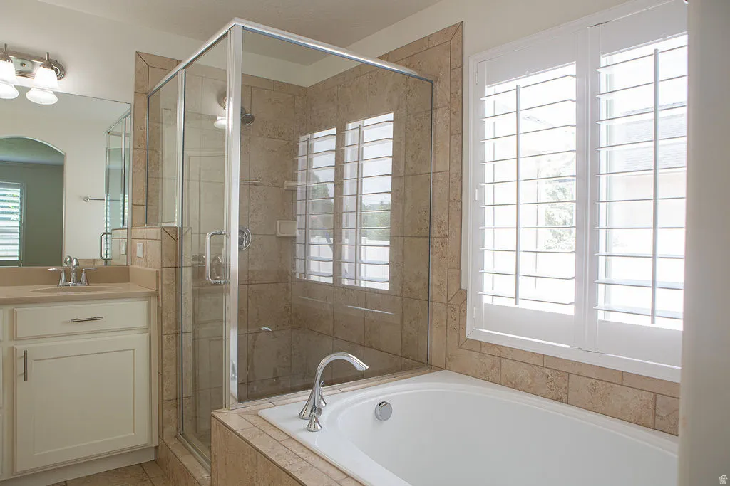 Bathroom featuring a glass-enclosed shower with tile surround, a separate soaking tub with deck-mounted faucet, and a single vanity with a solid surface countertop