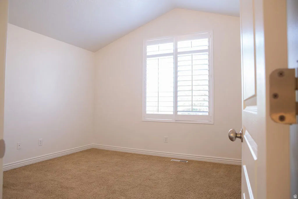 Carpeted room with vaulted ceilings and a window featuring white plantation shutters