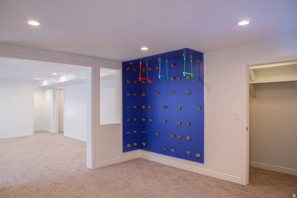Recreational wall feature with climbing holds and gymnastic rings, recessed lighting, neutral carpeting, and a built-in closet with shelving