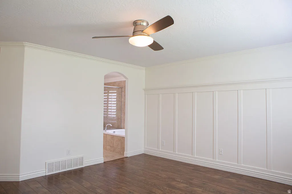Spacious room featuring wood-finish flooring, white board and batten wall paneling, crown molding, and a ceiling fan with integrated lighting