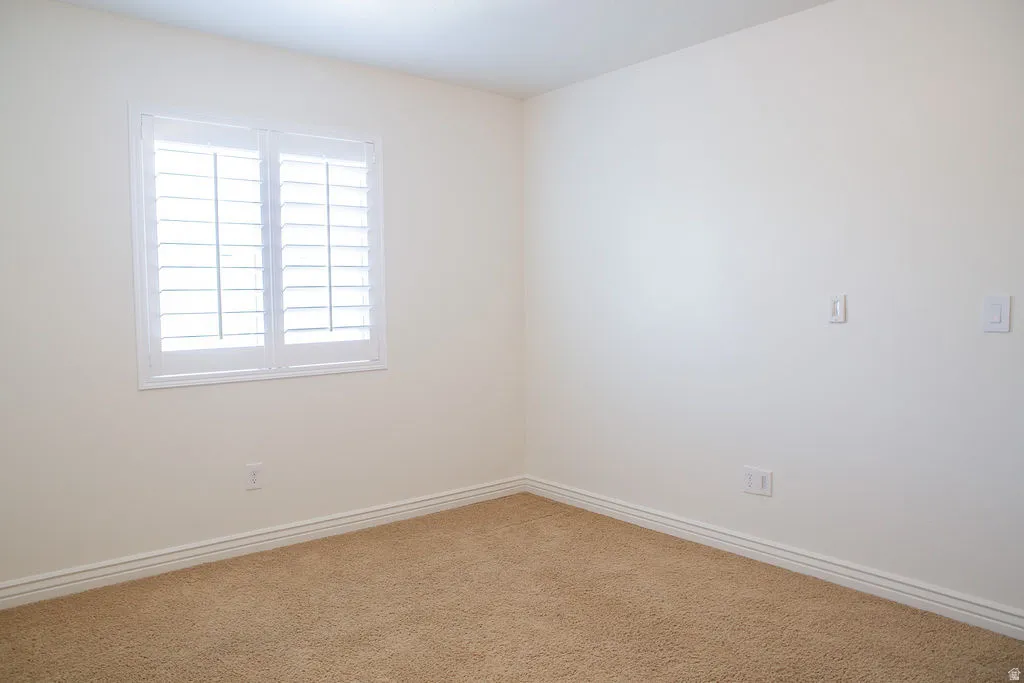 Bright room featuring a window with white plantation shutters, neutral wall color, and light brown carpeting