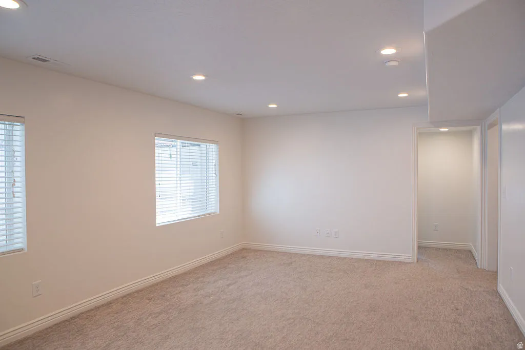 Spacious room featuring neutral carpet flooring, recessed lighting, two windows with blinds, and white trim