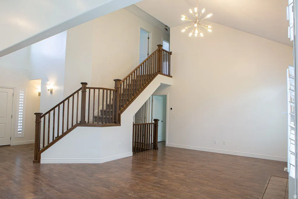 Vaulted ceiling entry featuring a chandelier, wood-finish flooring, and a staircase with wood railings