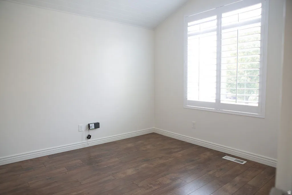 Bright room featuring a large window with white plantation shutters, wood-finish flooring, white baseboards, and a white ceiling with subtle texture