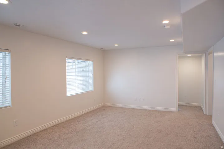 Spacious room featuring neutral carpet flooring, recessed lighting, two windows with blinds, and white trim