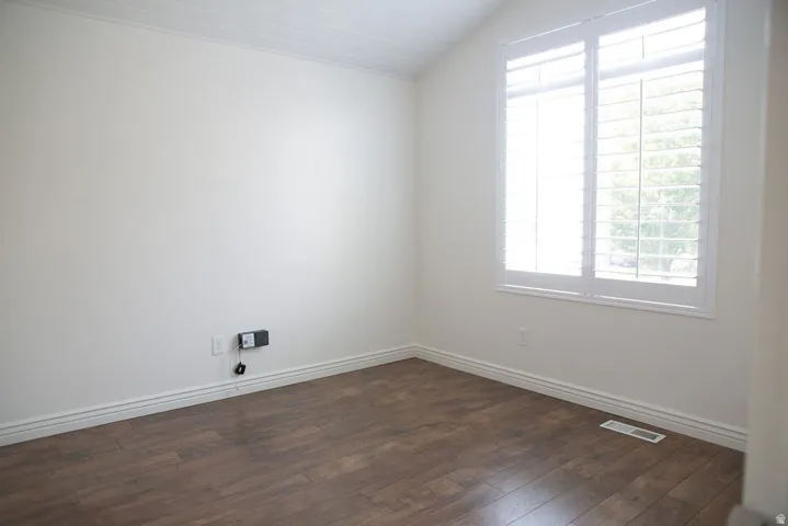 Bright room featuring a large window with white plantation shutters, wood-finish flooring, white baseboards, and a white ceiling with subtle texture