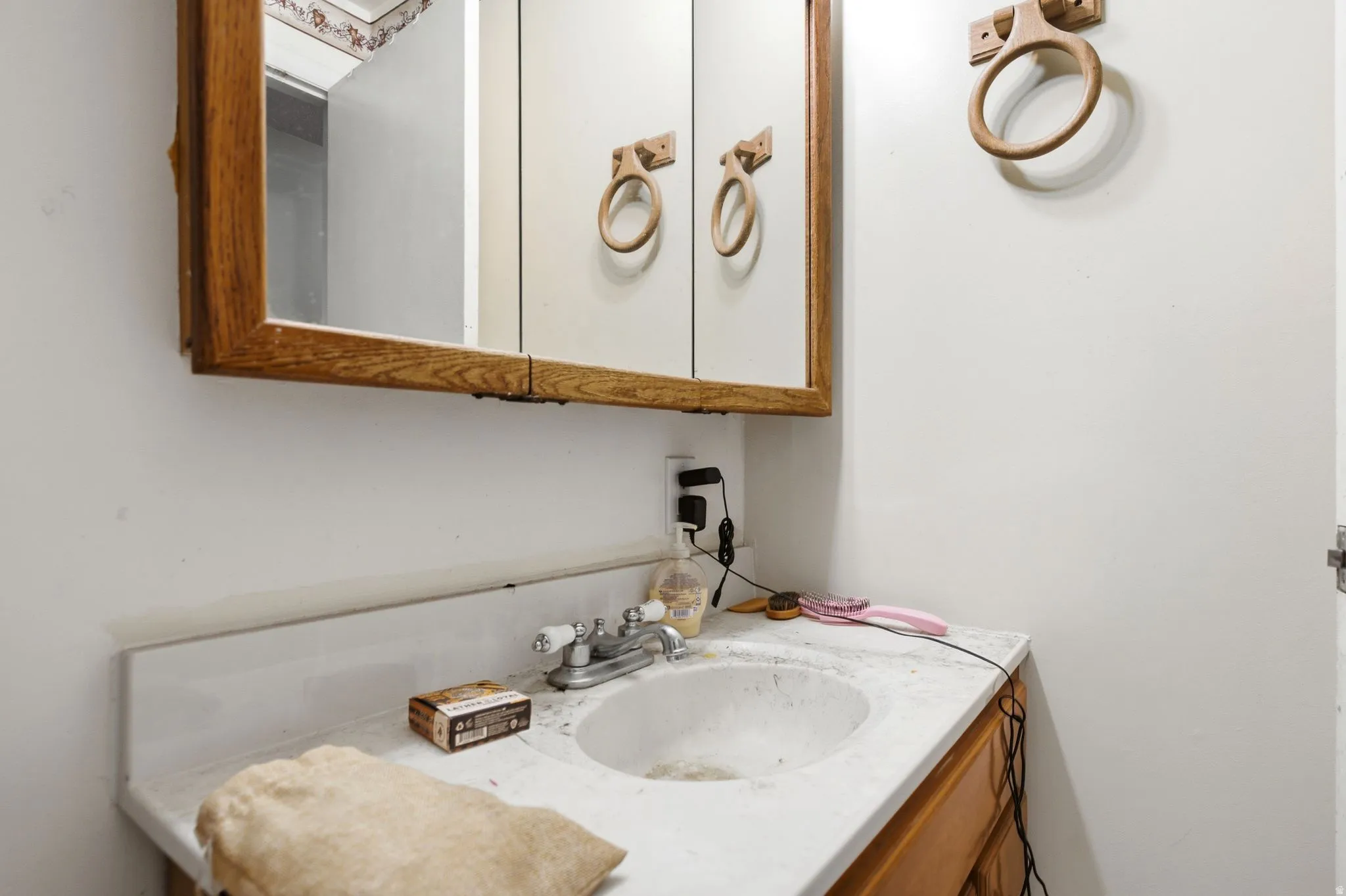 Wood-framed medicine cabinet with mirrored doors above a vanity featuring a white integrated sink and a two-handle faucet