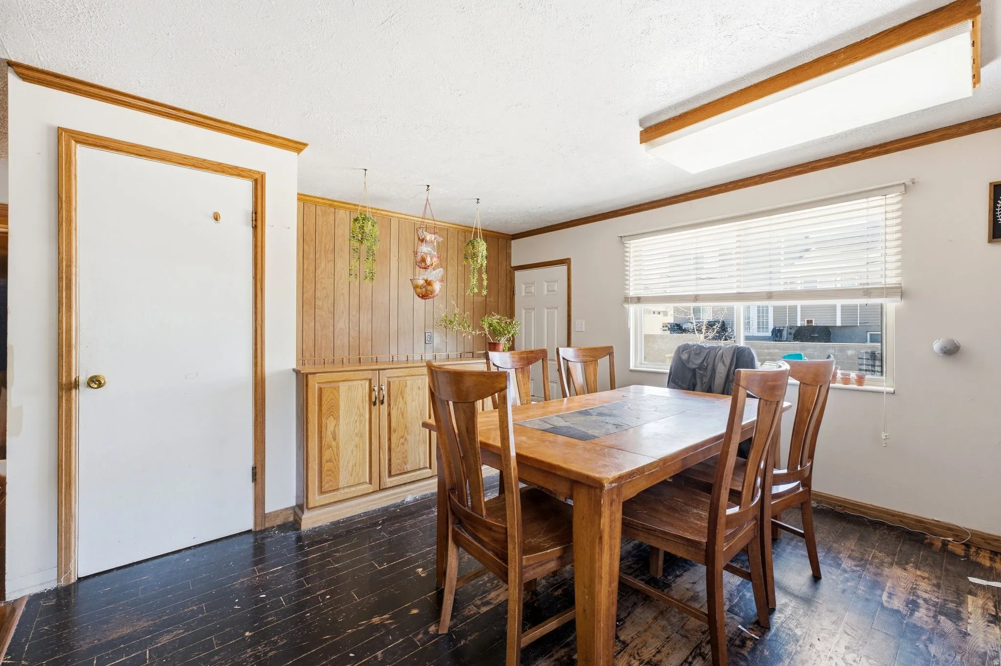 Dining area featuring wood-finish flooring, a built-in wood-finish cabinet with paneling, and a large window with blinds