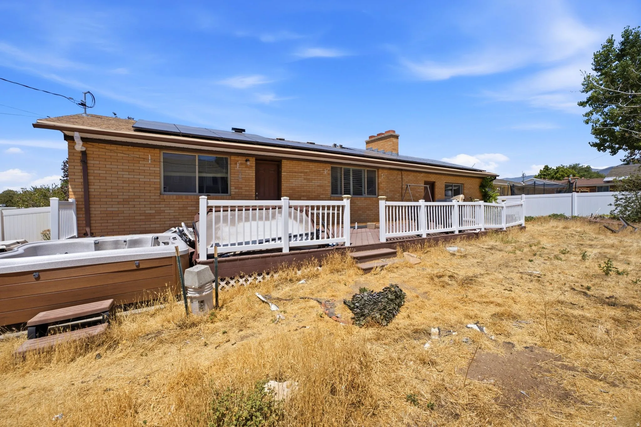 Rear exterior featuring brick siding, a wood-finish deck with white railings, and rooftop solar panels