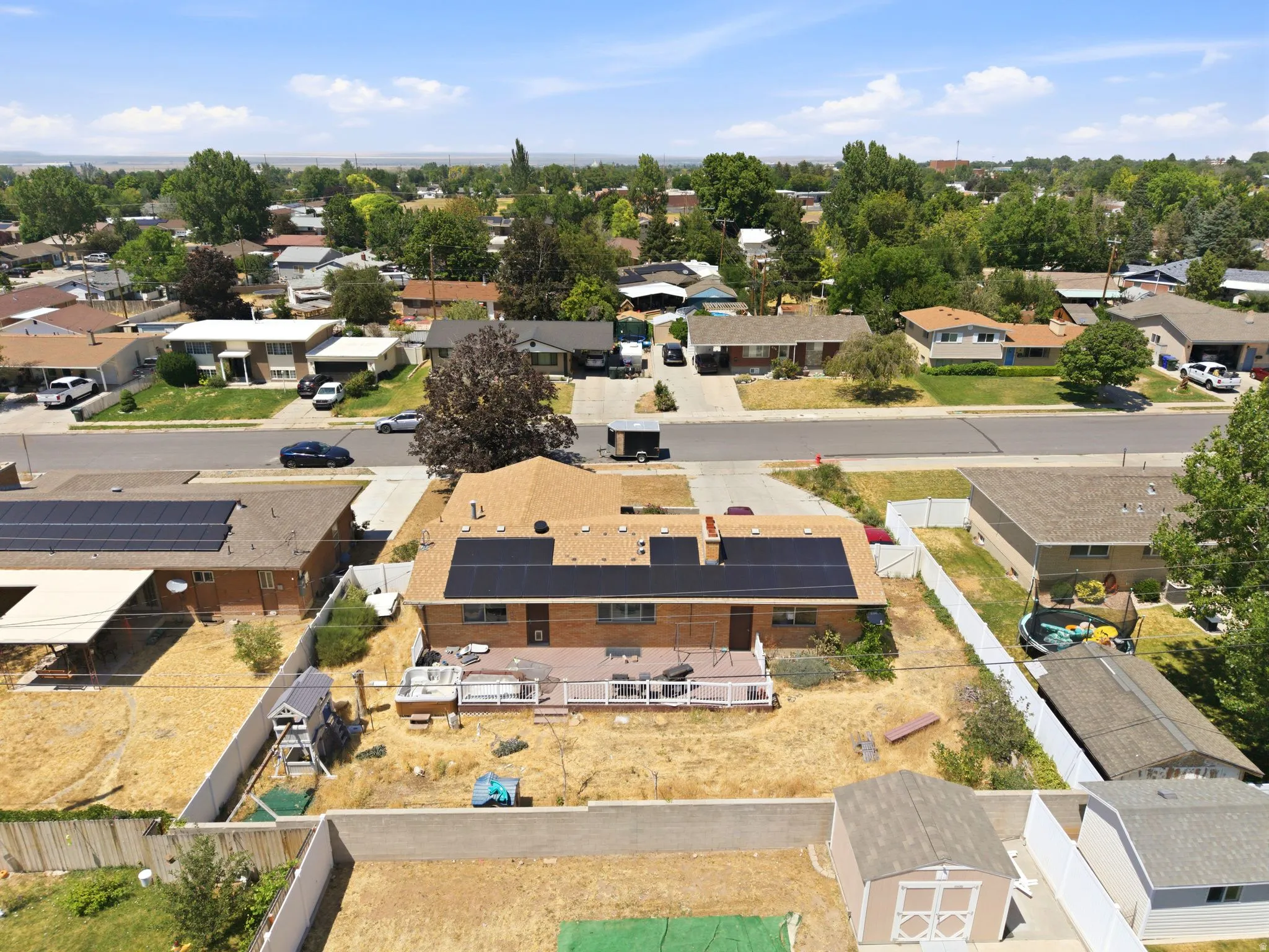 Rear exterior featuring a spacious composite deck, multiple solar panel arrays, and a brick facade
